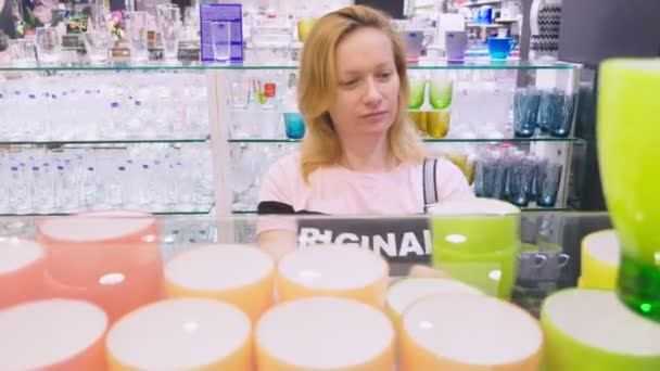 Una mujer compra platos en la tienda, examina varios artículos de platos . — Vídeo de stock