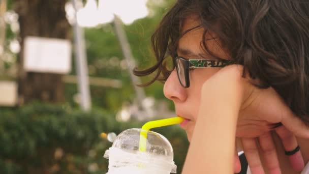 Втомився від спеки хлопчик п'є холодний коктейль через солому, крупним планом — стокове відео