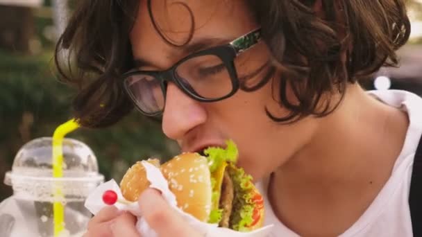 Tiener jongen hamburger en frietjes eten op terras. Close-up — Stockvideo