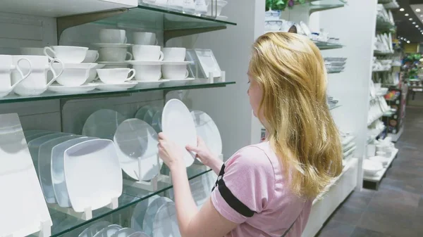 Una mujer compra platos en la tienda, examina varios artículos de platos . —  Fotos de Stock