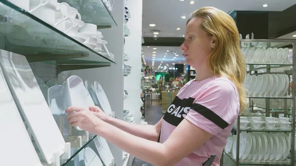 A woman buys dishes in the store, examines various items of dishes. — Stock Photo, Image