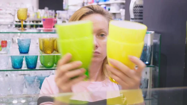 Una mujer compra platos en la tienda, examina varios artículos de platos . — Foto de Stock