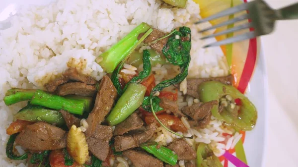 someone eats with a fork, rice with liver, top view food on a white dish.