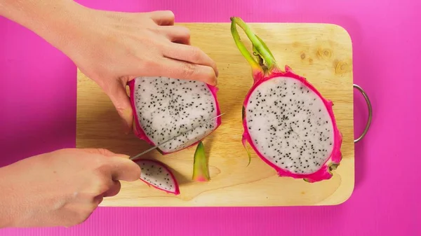 Vista dall'alto, mano femminile taglia il frutto con un coltello su una tavola di legno, frutta drago bianco. Il concetto di cibo sano naturale . — Foto Stock