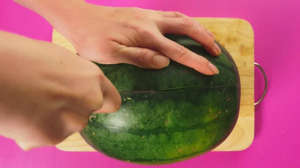 Vista superior, la mano femenina corta fruta con un cuchillo en una tabla de madera, sandía roja. El concepto de comida saludable natural . — Foto de Stock