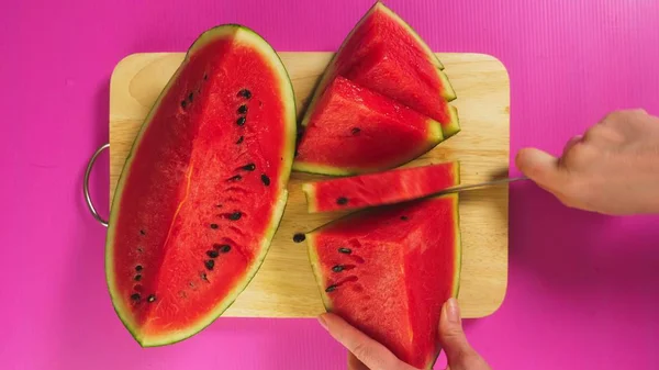 Vista dall'alto, mano femminile taglia frutta con un coltello su una tavola di legno, anguria rossa. Il concetto di cibo sano naturale . — Foto Stock