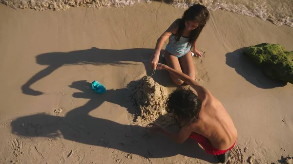 Подростки, брат и сестра строят песчаный замок на тропическом пляже — стоковое фото