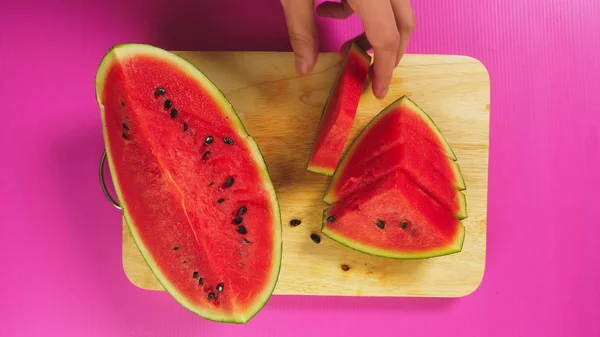 Vista superior, a mão feminina corta frutas com uma faca em uma tábua de madeira, melancia vermelha. O conceito de comida saudável natural . — Fotografia de Stock