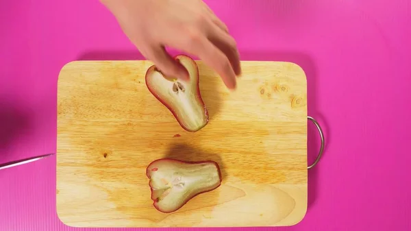 Vista superior, a mão feminina corta um fruto com uma faca em uma tábua de madeira, aumentou a maçã, chompu. O conceito de comida saudável natural . — Fotografia de Stock