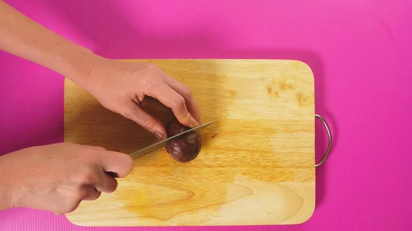 Vista superior, la mano femenina corta fruta con un cuchillo en una tabla de madera, maracuya. El concepto de comida saludable natural . — Foto de Stock
