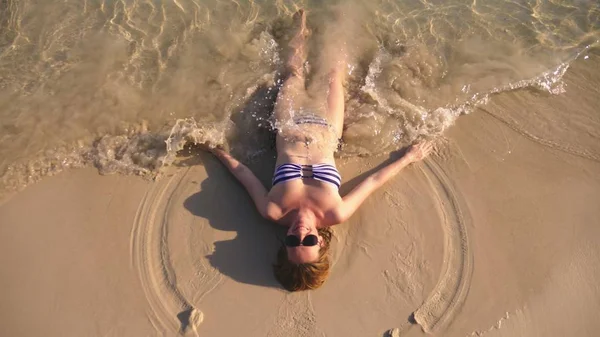 Fille blonde en maillot de bain et lunettes de soleil noires sur une plage de sable blanc au bord de l'océan en vacances. Beau modèle avec corps sexy nage dans l'eau de mer bleue — Photo