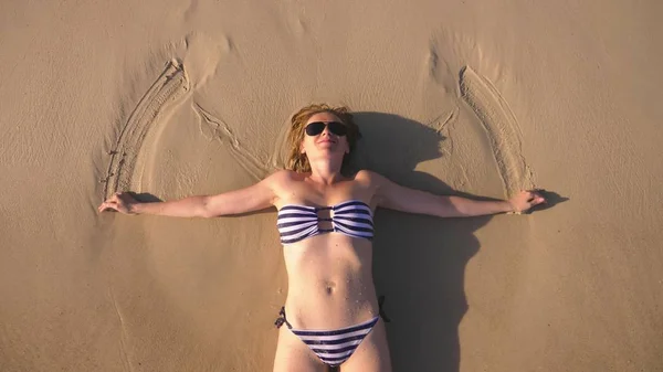 Blond flicka i en baddräkt och svarta solglasögon på en vit sandstrand vid havet semester. Vacker modell med sexig kropp simmar i blå havsvatten — Stockfoto