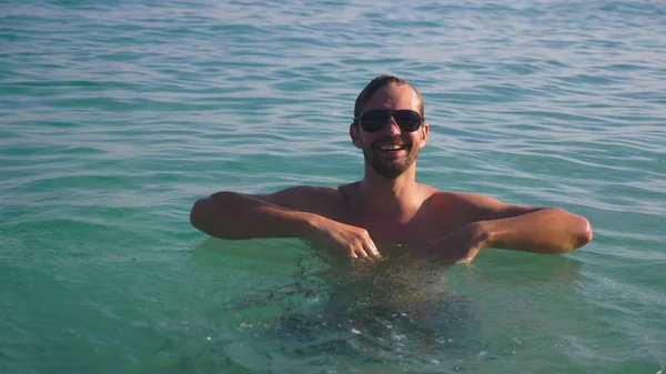 Retrato de um jovem bonito com barba em óculos de sol relaxado em água cristalina do mar — Fotografia de Stock