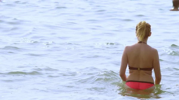 Chica rubia en traje de baño y gafas de sol negras. mujer en traje de baño rojo camina hacia el mar — Foto de Stock