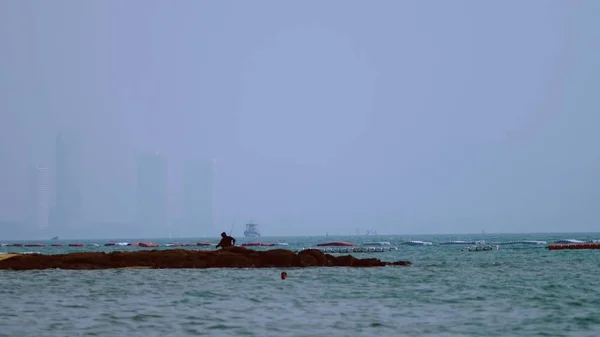 Silhuetten av en fiskare med ett fiskespö mot bakgrund av staden och fartyg. — Stockfoto
