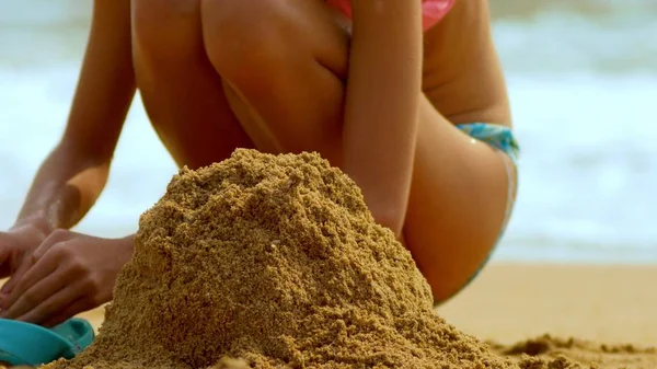 Chica construye un castillo de arena en una playa tropical. primer plano — Foto de Stock