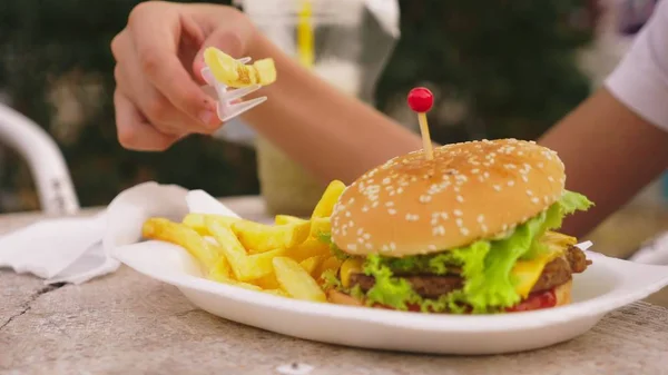 Teen chłopiec jedzenie hamburger i frytki w kawiarni na świeżym powietrzu. szczelnie-do góry — Zdjęcie stockowe