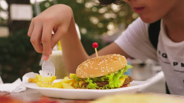 Teenie-Junge isst Hamburger und Pommes im Outdoor-Café. Nahaufnahme — Stockfoto
