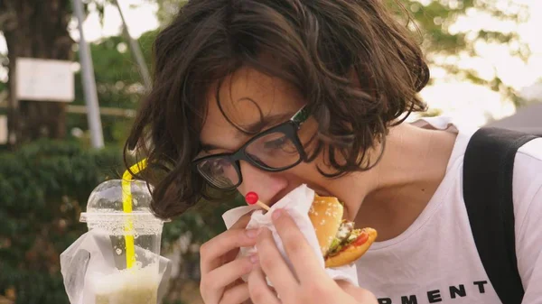 Teen boy eating hamburger and french fries in outdoor cafe. close-up — ストック写真