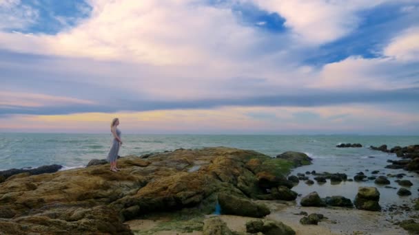 Giovane donna che cammina su una roccia e gode della vista del tramonto, spruzzando onde — Video Stock