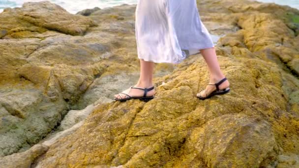 Nahaufnahme. Frauenbeine in Sandalen und langem grauen Rock stehen bei Ebbe am felsigen Meeresufer. — Stockvideo