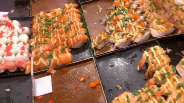 Cocina asiática, concepto de comida. Cerca. manos con pinzas elegir sushi en el mercado nocturno en la calle . — Vídeos de Stock