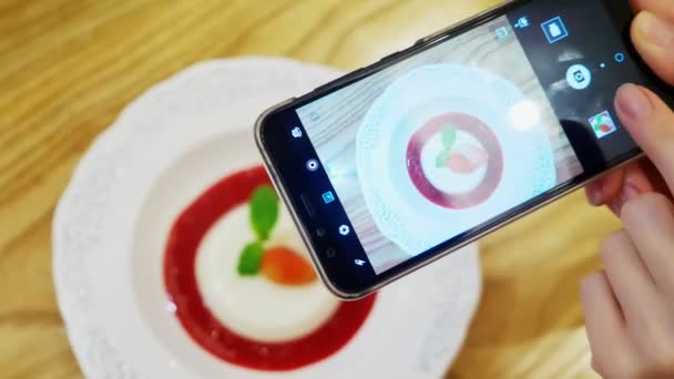 Primer plano. Las manos femeninas toman fotos del postre de panna cotta en un teléfono inteligente en un restaurante . — Vídeos de Stock