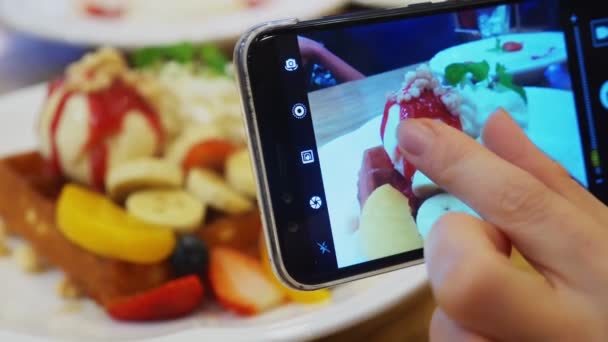 Close-up. Vrouwelijke handen Neem een foto van een dessert van Weense wafels, ijs en vers fruit op een smartphone in een restaurant. — Stockvideo