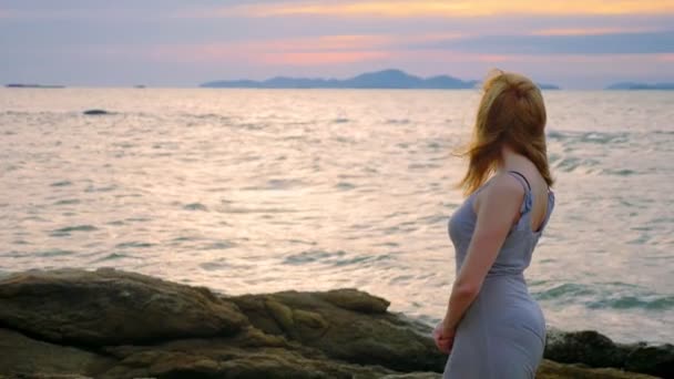 Young woman walking on a rocky and enjoying the view of the sunset, splashing waves — Stock Video