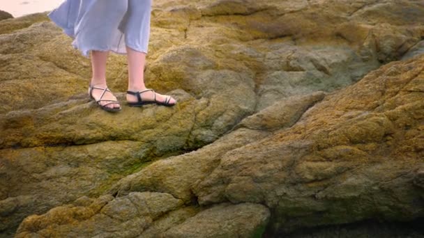 特写。在低潮时, 穿着凉鞋和长长的灰色裙子的妇女腿在岩石的海滨. — 图库视频影像