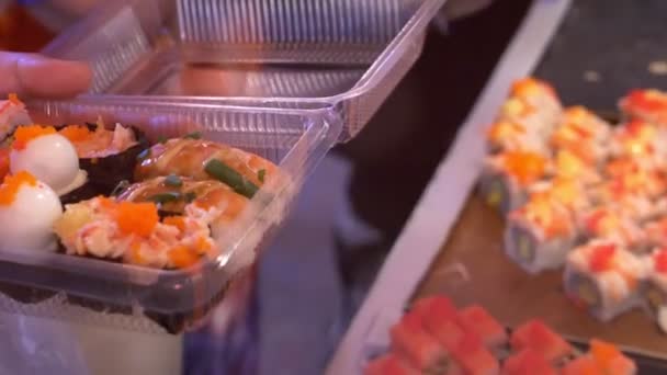 Cocina asiática, concepto de comida. Cerca. manos con pinzas elegir sushi en el mercado nocturno en la calle . — Vídeos de Stock