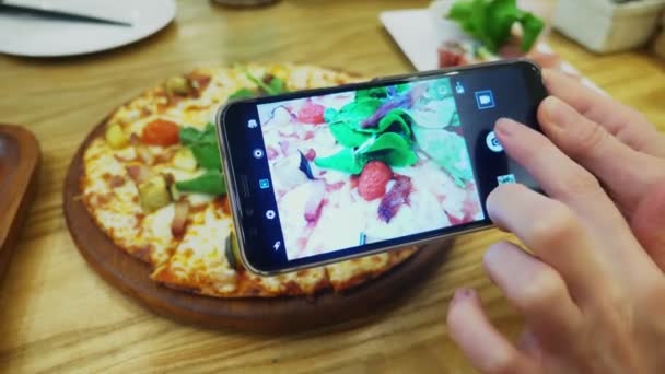 Close-up. Vrouwelijke handen neem foto van pizza op smartphone in restaurant. — Stockvideo