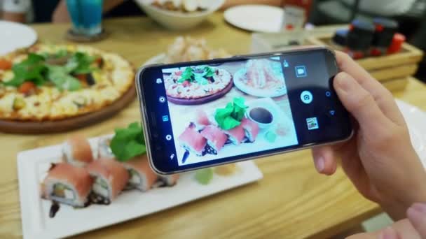 Close-up. Mãos femininas tiram uma foto de sushi em um smartphone em um restaurante . — Vídeo de Stock