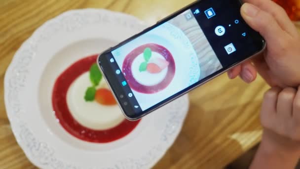 Close-up. Female hands take photo of panna cotta dessert on a smartphone in a restaurant. — Stock Video