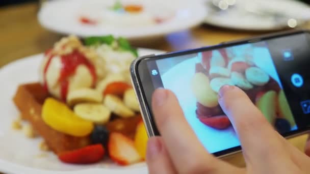 detail. Ženské ruce vyfotit dezert vídeňské vafle, zmrzlinou a čerstvým ovocem na smartphone v restauraci.