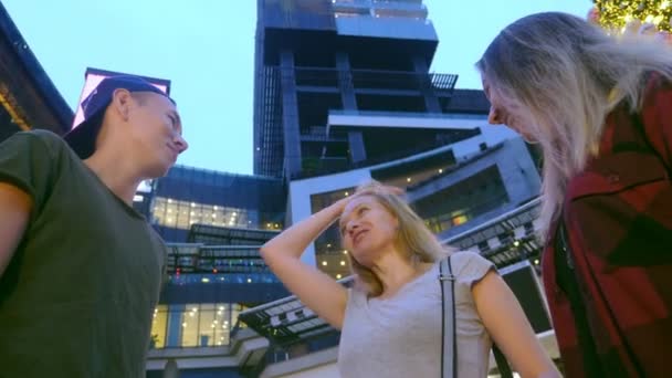 Tre vänner, asiater och kaukasier kommunicera på kvällen på gatan av den moderna staden. — Stockvideo