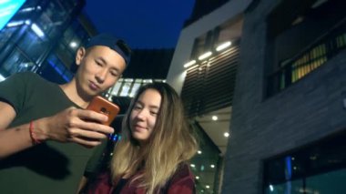 mutlu Genç Asyalı çift erkek ve kız arkadaşı. bir semt akşamları cadde üzerinde duran bir akıllı telefon kullanma.