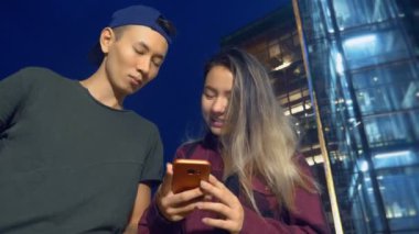 mutlu Genç Asyalı çift erkek ve kız arkadaşı. bir semt akşamları cadde üzerinde duran bir akıllı telefon kullanma.