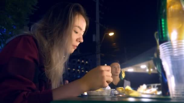 Νέοι Ασιατικές κορίτσι τρώει το φαγητό του δρόμου σε υπαίθρια διανυκτέρευση. — Αρχείο Βίντεο