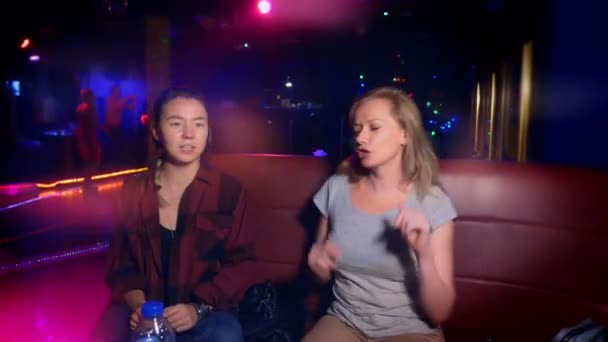 Twee jonge vrouwen Aziatische en Kaukasische aan een tafel in een discotheek te glimlachen — Stockvideo