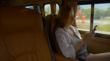 bir minibüs yolcu koltuğunda otururken bir kadının telefon kullanır.