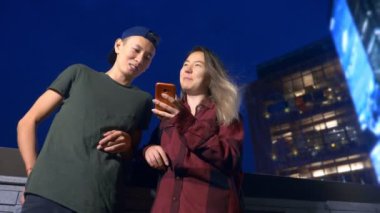 mutlu Genç Asyalı çift erkek ve kız arkadaşı. bir semt akşamları cadde üzerinde duran bir akıllı telefon kullanma.
