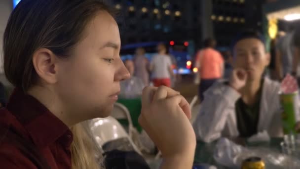 Junge asiatische Mädchen essen Streetfood in der Nacht im Freien. — Stockvideo