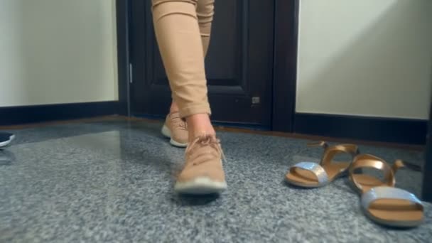 Close-up. vrouwelijke benen in sneakers. een vrouw loopt in een huis en wandelingen verleden schoenen verspreid door kinderen en haar man — Stockvideo