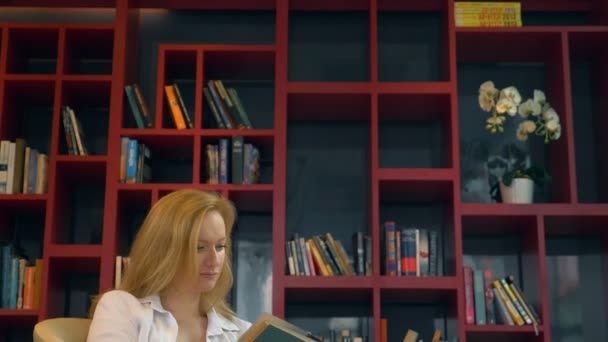 Jovem mulher lendo um livro na biblioteca no fundo de estantes — Vídeo de Stock