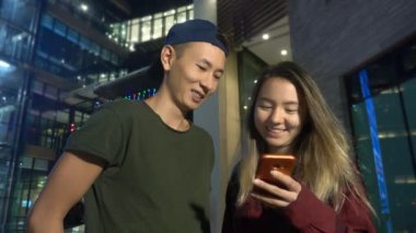 mutlu Genç Asyalı çift erkek ve kız arkadaşı. bir semt akşamları cadde üzerinde duran bir akıllı telefon kullanma.
