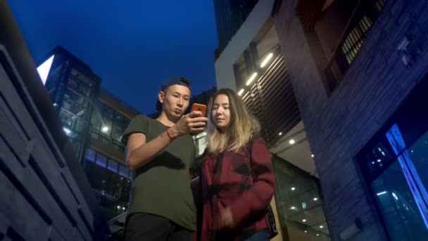 Feliz jovem asiático casal namorado e namorada. usar um smartphone enquanto estiver de pé em uma rua da cidade à noite . — Vídeo de Stock