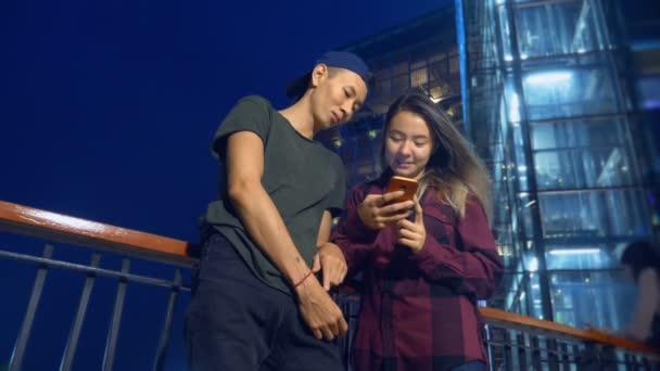 Счастливая молодая азиатская пара парень и девушка. использовать смартфон, стоя на городской улице вечером . — стоковое видео