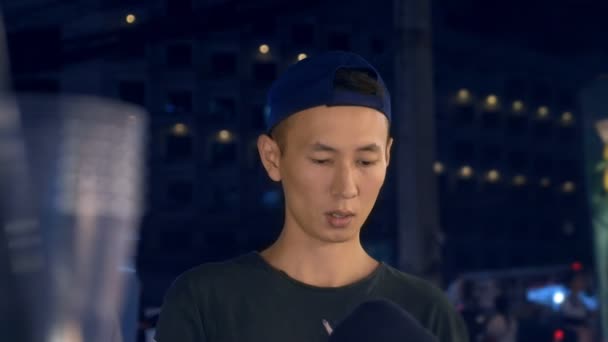 Красивый молодой азиат по вечерам курит сигарету на улице. на фоне оживленной городской улицы, размытие — стоковое видео