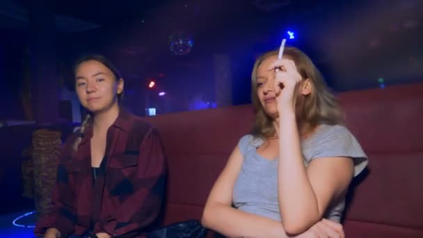 Dwa uśmiechnięte młode kobiety azjatyckiej i rasy kaukaskiej przy stole w nocnym klubie — Wideo stockowe